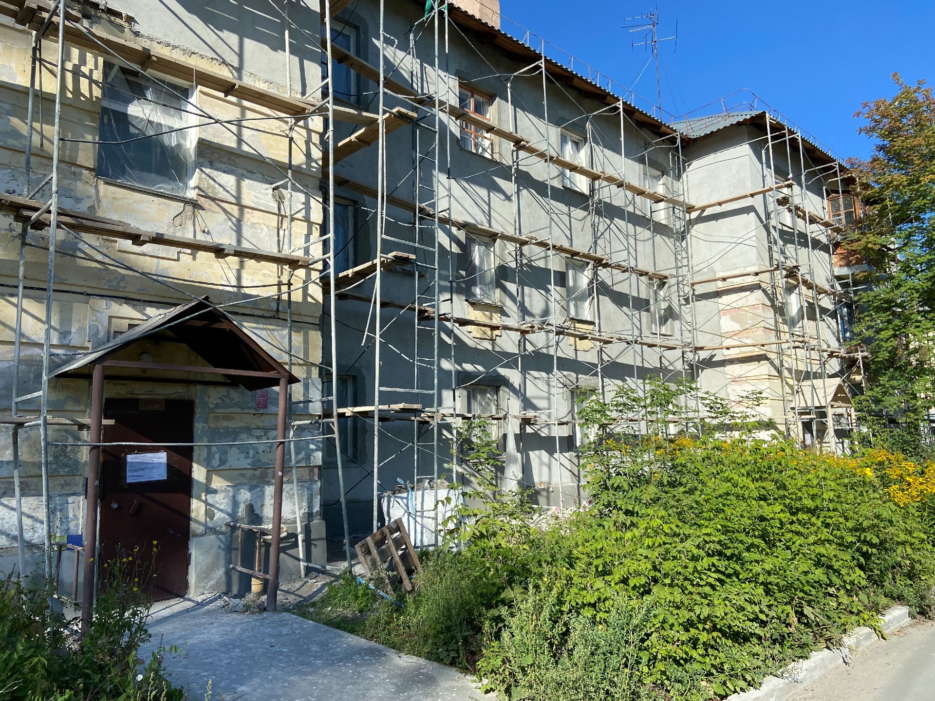 Painting and Plastering Exterior House Scaffolding Wall. Home Facade Insulation, Stucco and Painting Works During Exterior Wall Renovations and Repair Outdoors.